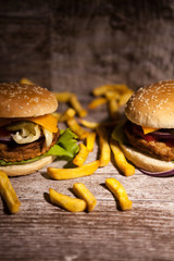 Tasty burgers on wooden plate next to fries. Fast food. Unhealthy snack