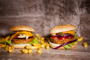 Tasty burgers on wooden plate next to fries. Fast food. Unhealthy snack