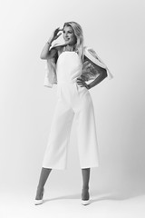 Beautiful pretty stylish blond woman with medium length straight hair posing in white overall and jacket on white background. Bright fashion full length studio portrait