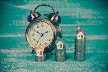 mini house on coin stack with alarm clock.