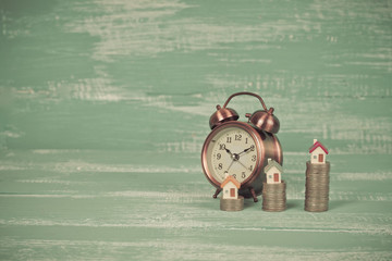 mini house on coin stack with alarm clock