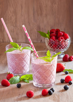 Tasty blueberry, strawberry, raspberry and yogurt smoothies with berries and mint around on wooden background