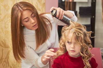 Stylist working with child, hairspray. Cute little girl, hair salon.