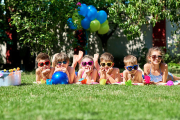 Fototapeta premium Group of children in sunglasses smiling lies on grass in summer.