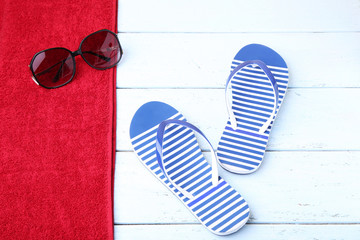 Pair of flip flops with towel and sunglasses on wooden table