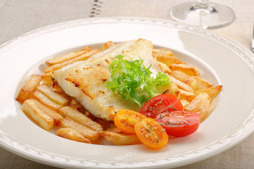Fried cod fillet on a white plate and french fries
