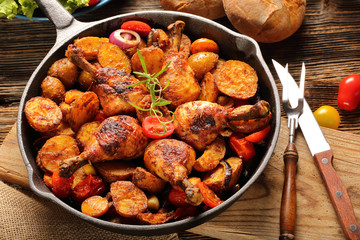 Roasted chicken legs with baked potato on frying pan