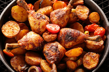 Roasted chicken legs with baked potato on frying pan