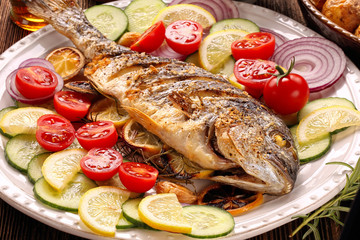 Roasted dorada fish with vegetables on wooden background