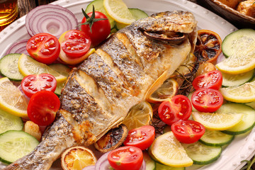 Roasted dorada fish with vegetables on wooden background