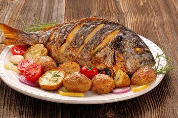 Roasted dorada fish with vegetables on wooden background