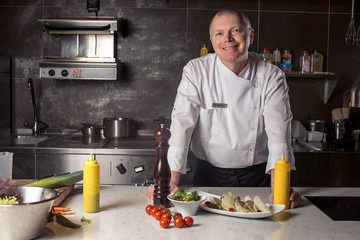 Portrait of a smiling male chef with cooked food standing in the kitchen