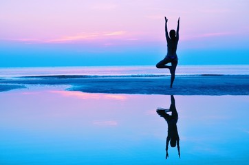 Silhouette woman practicing yoga on the beach at sunset.