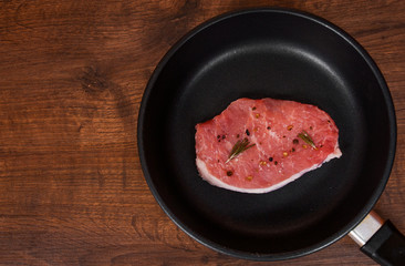 raw meat steak on cast iron frying pan on the brown wooden table background. rustic kitchen table with copy space. top view.