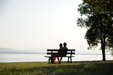 Naklejka na ściany i meble Couple in love sitting on a bench by the lake