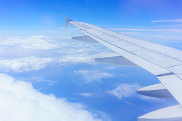 Fototapeta na wymiar Looking thru airplane 's window seeing wing of airplane , white clouds and blue sky