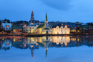 Beautiful reflection of the cityscape of Reykjavik in lake Tjornin at the blue hour in winter
