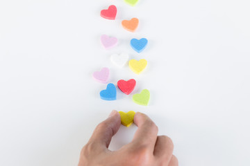 Hand is putting colorful hearts on white background, love concept