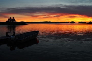 Amazing vivid colors sunset over a lake with a deck, a boat and a small island in Canada