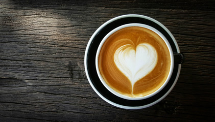 Heart shape of latte art coffee in black cup on old wooden background,top view and copy space with sunlight