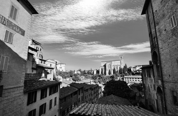 Black and white urban vista of traditional homes in Siena, Italy with Basilica san Domenico in the background