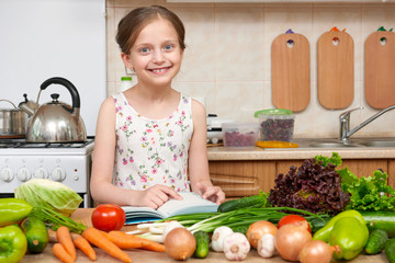 child girl with fruits and vegetables in home kitchen interior, read cooking book, healthy food concept