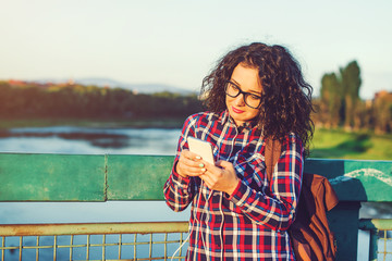 Smiling young woman or teenage girl with smartphone and headphones listening to music outdoors.