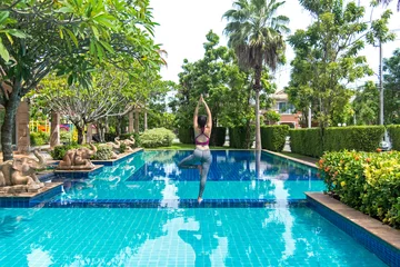 Keuken spatwand met foto Asia woman doing yoga fitness exercise for relax and healthy beside swimming pool background.  Healthy Concept. © freebird7977
