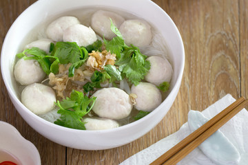 White noodle with pork ball soup in white bowl with seasoning on brown wooden floor  thai food / Still Life food, selective focus .