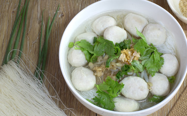 White noodle with pork ball soup in white bowl with seasoning on brown wooden floor  thai food / Still Life food, selective focus and space for text.