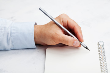 Lefty writes in empty notebook on white table. International Lefthanders Day.