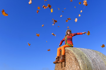 A young child jumps up high and feels joyful about  autumn arriving. She throws colored leaves in the air  and expresses her happiness. 