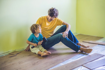 Father and son installing new wooden laminate flooring. infrared floor heating system under...
