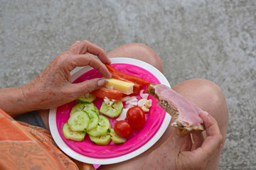 Senior holding bread with ham and vegetable plate