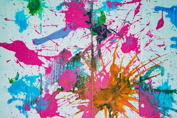 Abstract pink, orange, green and blue paint splashes on wood panel background