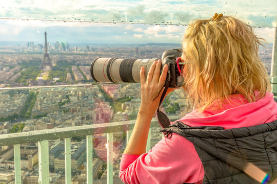 Traveler photographer takes photos of Tour Eiffel from observation deck of Tour Montparnasse. Woman photographer in French capital, Europe. Paris cityscape. Popular travel destination concept.