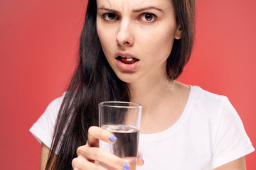Beautiful young woman on a red background drinking a pill