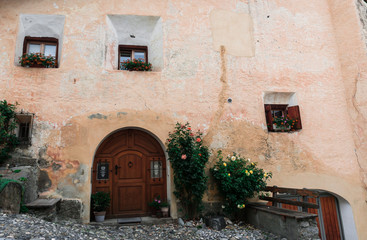 Fototapeta na wymiar house front in the typical Engadin architecture style with a wooden arched doorway and flower pots and a wooden bench