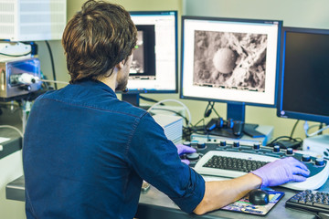 Scientist works at a electron microscope control pannel with two monitors in front of him