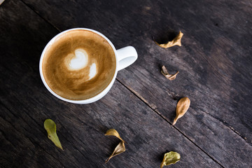Cup of coffee on wooden table with dry leave