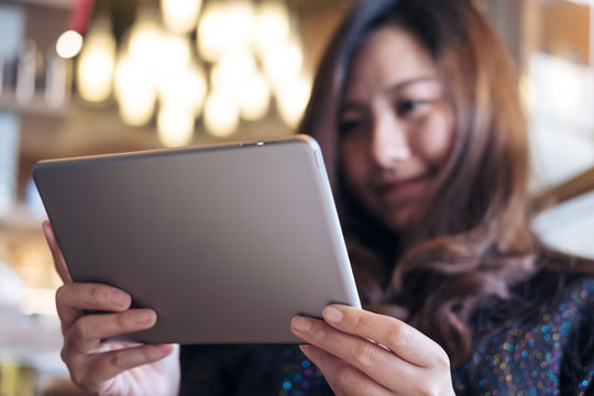A beautiful Asian woman with smiley face holding and using tablet pc in modern cafe