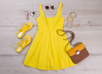 Yellow dress with accessories on a wooden background.