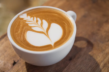 Top view of hot coffee cappuccino latte art in white ceramic cup on wooden plate