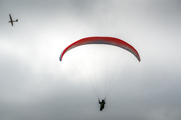 A hang glider and a plane in the sky
