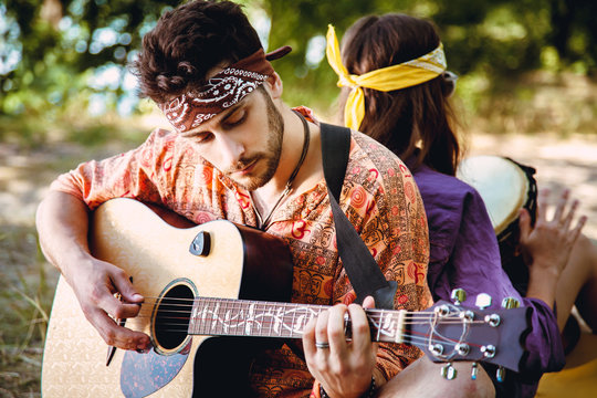 Beautiful young couple in love in hippie style rest on the nature. A man plays the guitar and the girl plays the drum