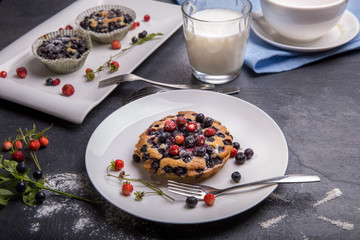 Berry muffin with blueberries and strawberries on a white plate and a wooden table served with milk and and fresh berries