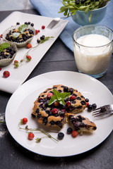 Berry muffin with blueberries and strawberries on a white plate and a wooden table served with milk and and fresh berries