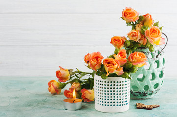 Fresh orange roses flowers in mint vase and lit candle