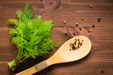 Bunch of fresh dill and a wooden spoon with peppercorns on wooden background. Top view