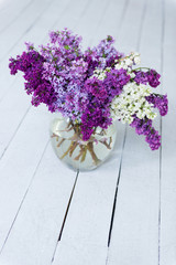 Fototapeta na wymiar A bouquet of fresh lilac flowers in a glass vase on a wooden floor.